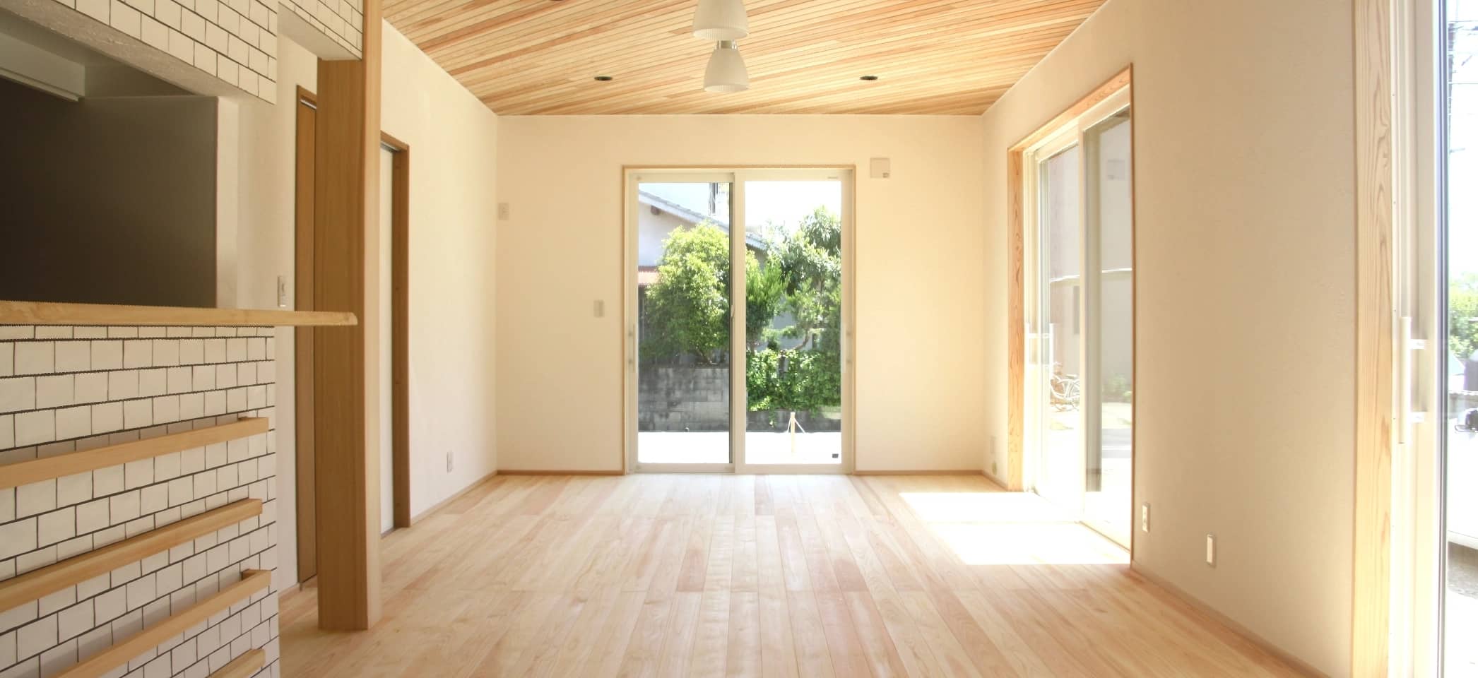 やさしい木の枠や床、棚が印象的な部屋に窓から光が入っている風景。外には木が見える。