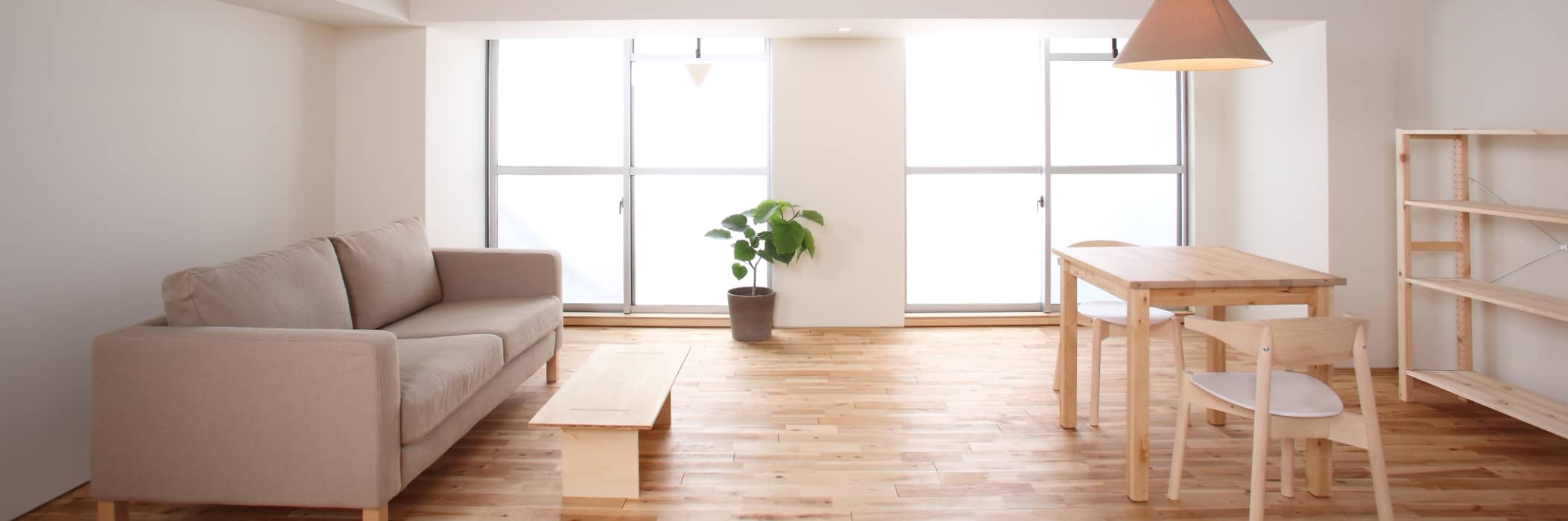 白の壁にブラウンのソファーや木の机が置かれているお部屋の風景